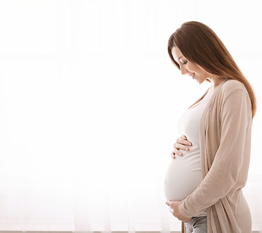 Photo of a pregnant woman smiling holding her stomach