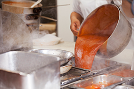 A person pouring a pot of sauce into shallow containers to cool.