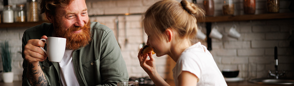 Father drinking a cup of coffee while daughter eats donut
