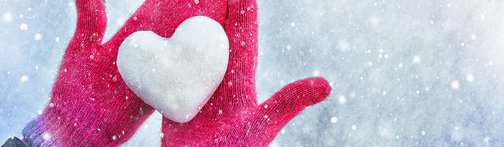 Mitted hands holding a snow heart in a snowfall