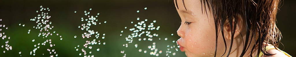 A small children drinking water from a sprinkler