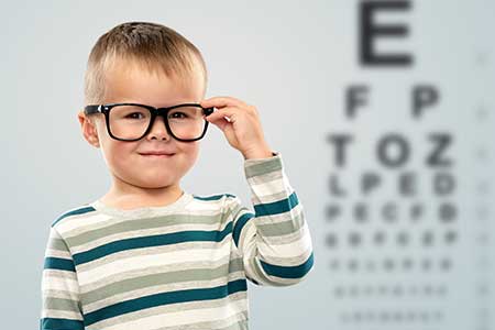 Child wearing glasses, standing in front of eye test chart