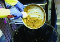 A person scraping left over food in a bowl into the garbage