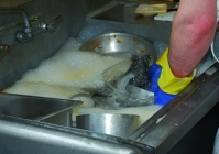 A person washing dishes in the first compartment sink.