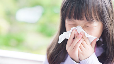 Photo of a girl sneezing into a tissue