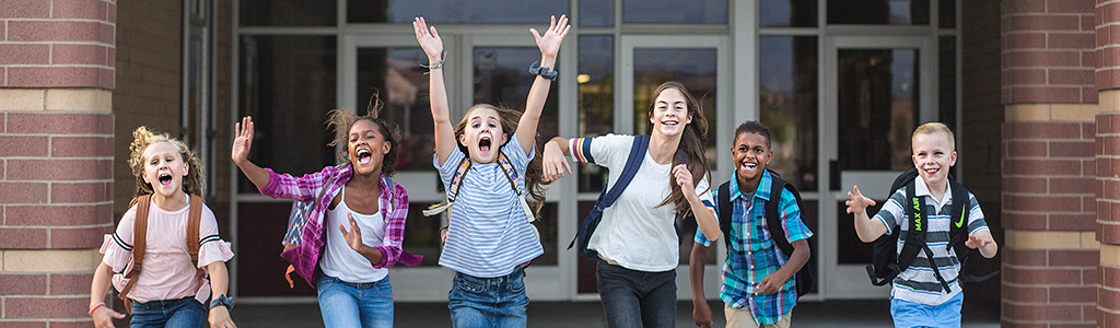 Group of children excitedly running in front of their school