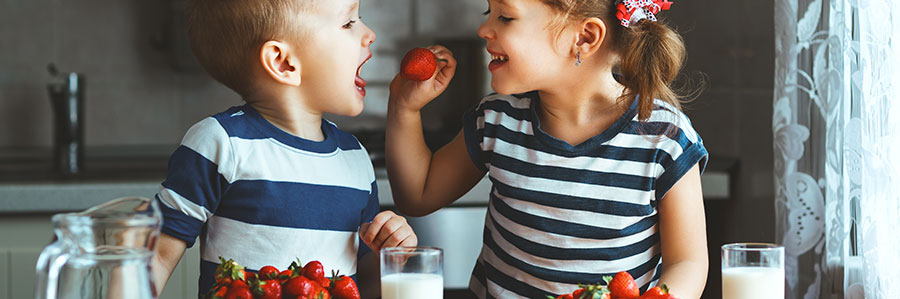 young girl feeding her younger brother a strawberry 