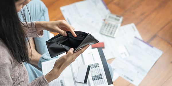 Photo of a woman looking at an empty wallet surrounded by bills